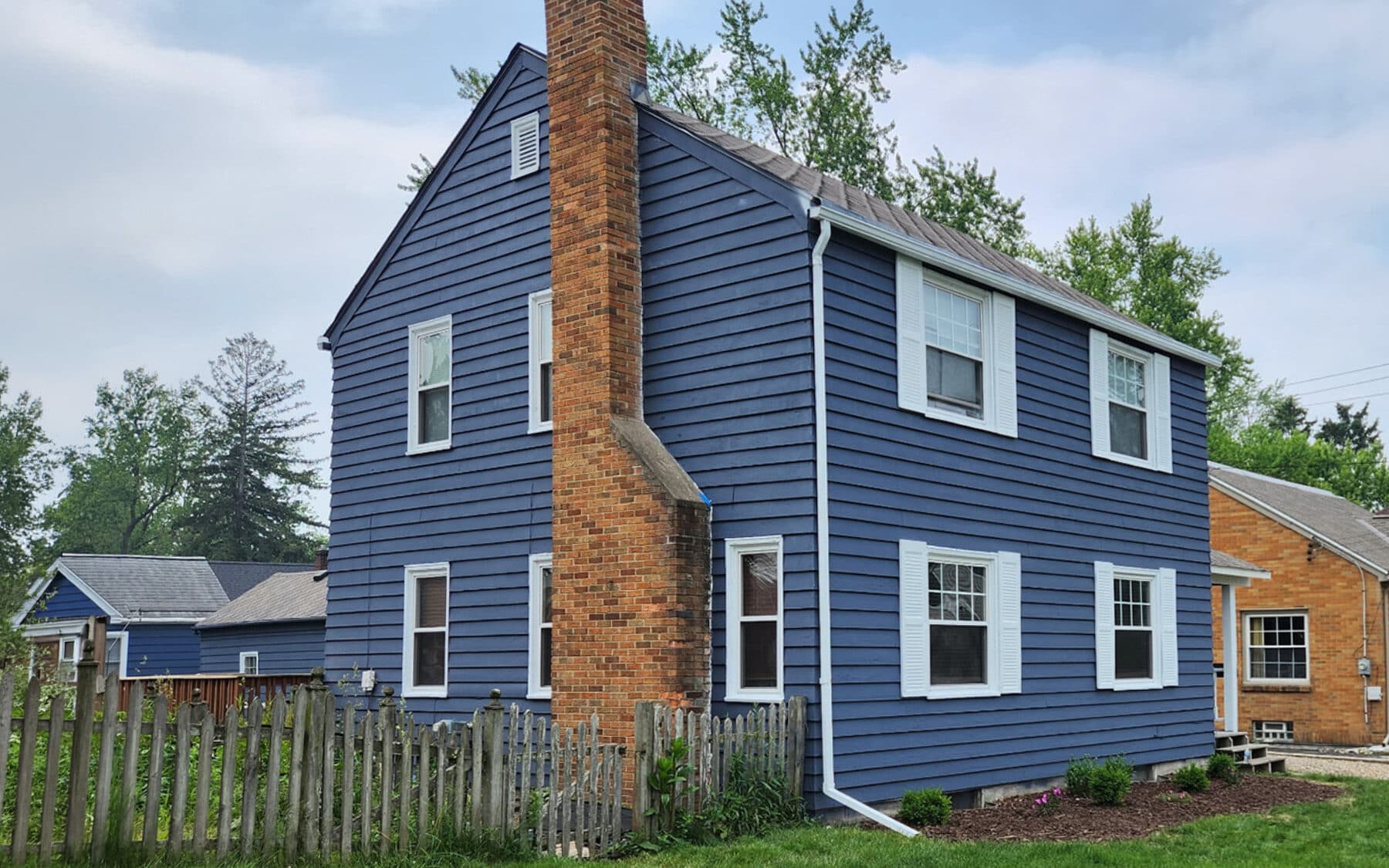 Side view of colonial home repainted navy blue with white trim and preserved brick chimney by Fortoso Painting in Kalamazoo, Michigan