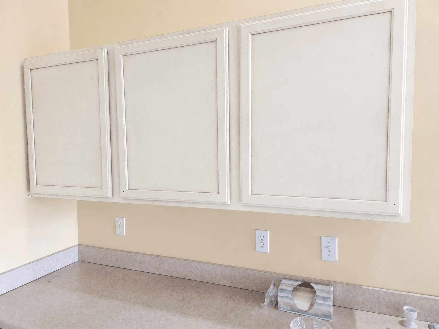 Three white cabinet doors mounted above a counter before refinishing by Fortoso Painting in Vicksburg, Michigan