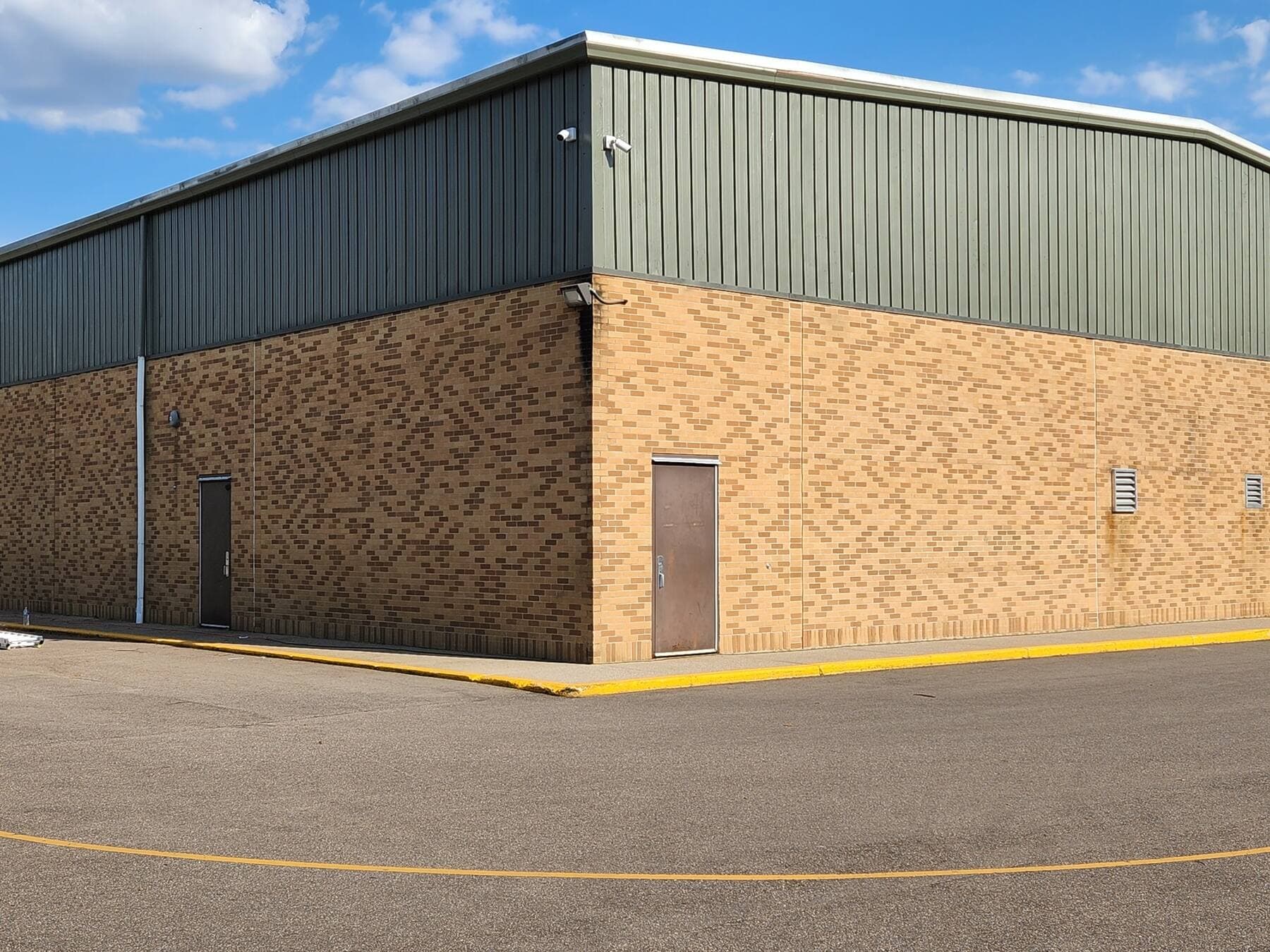 Same industrial facility from a corner angle showing the brick base and dark green metal upper siding meeting, repainted by Fortoso Painting in Southwest Michigan