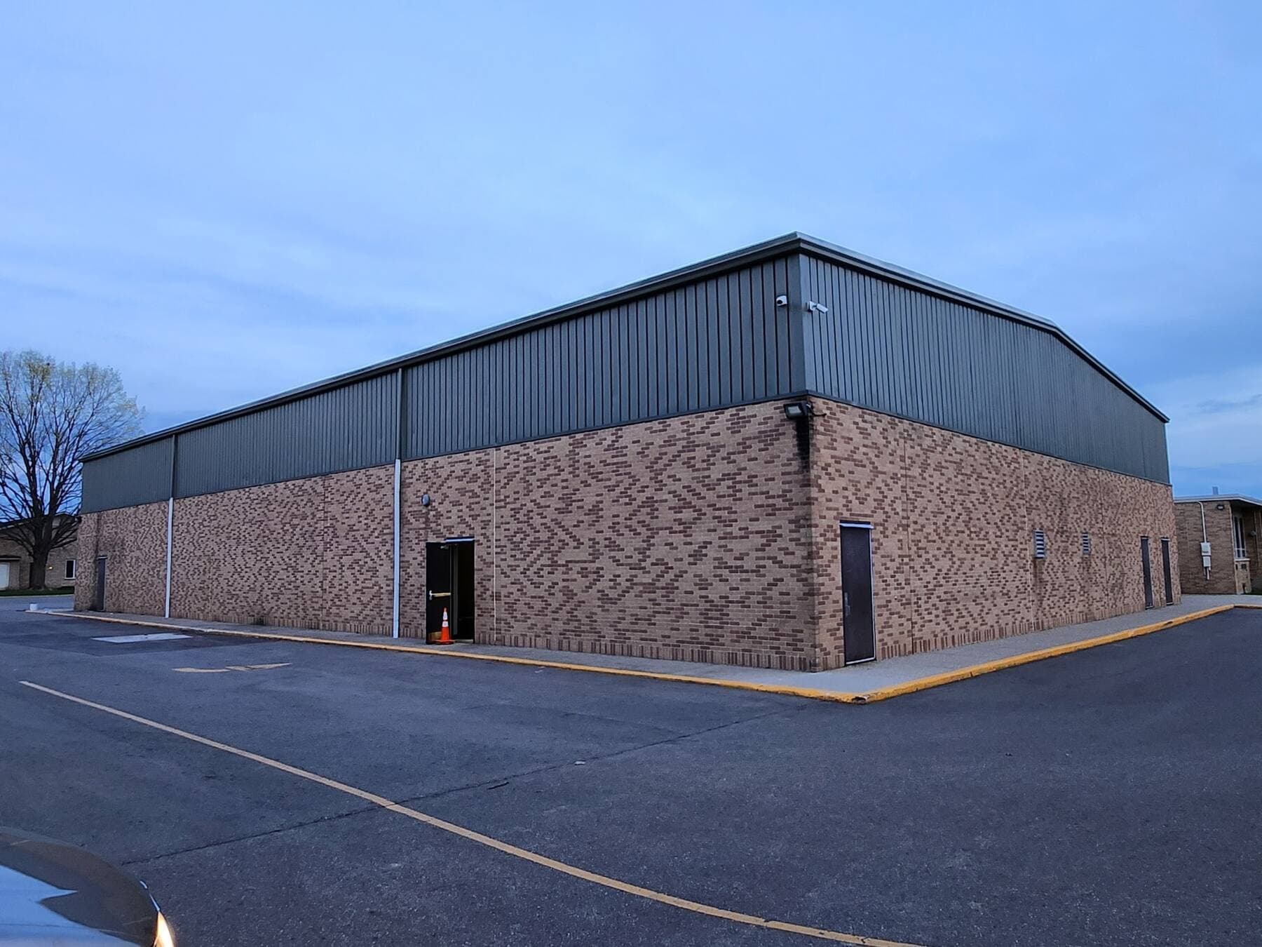 Industrial facility with brick base and dark green metal upper siding, long elevation view, repainted by Fortoso Painting in Southwest Michigan