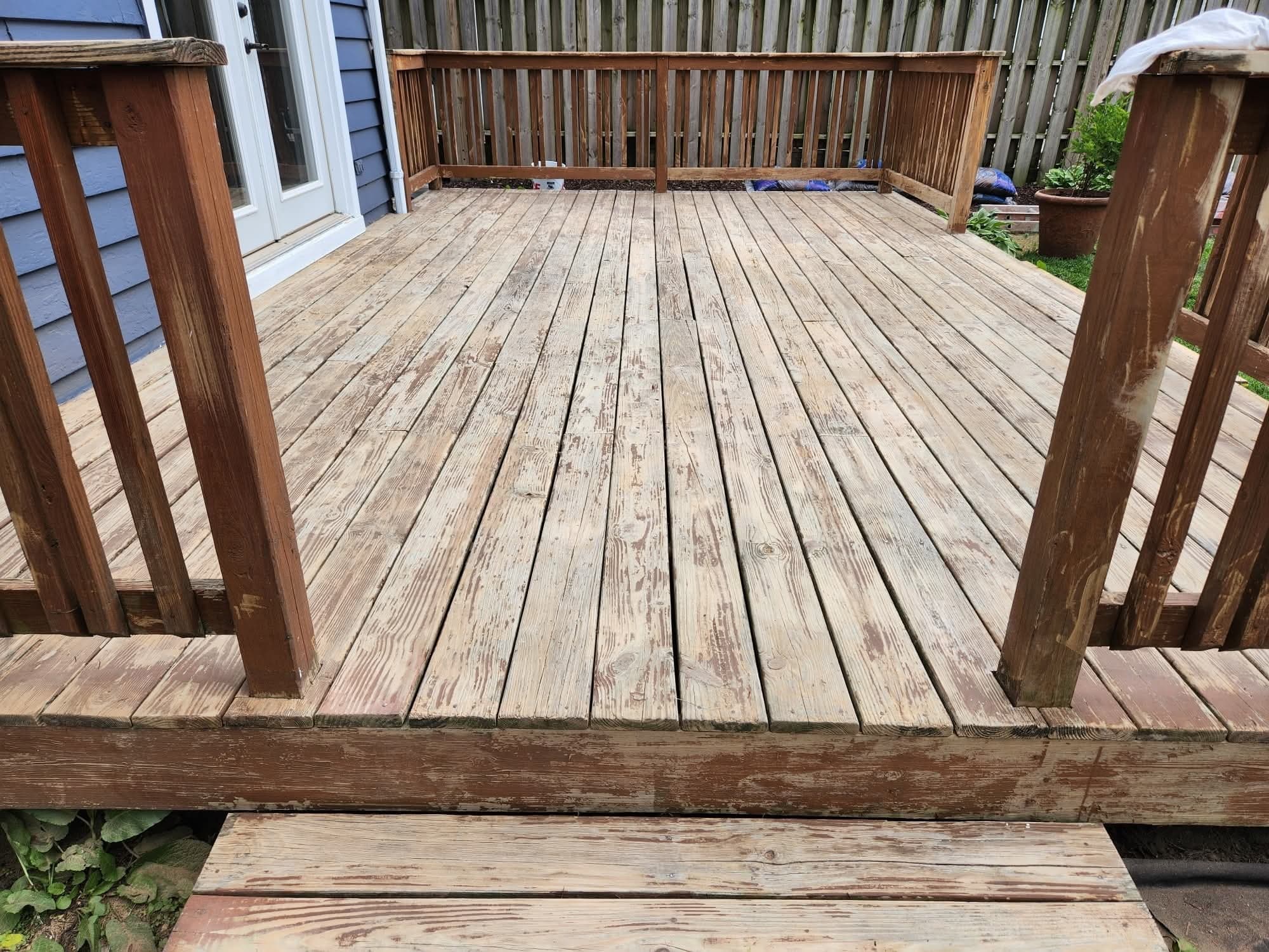 Weathered, sun-bleached wood deck with dried-out tan planks and railing attached to a navy blue home before deck staining by Fortoso Painting in Portage, Michigan