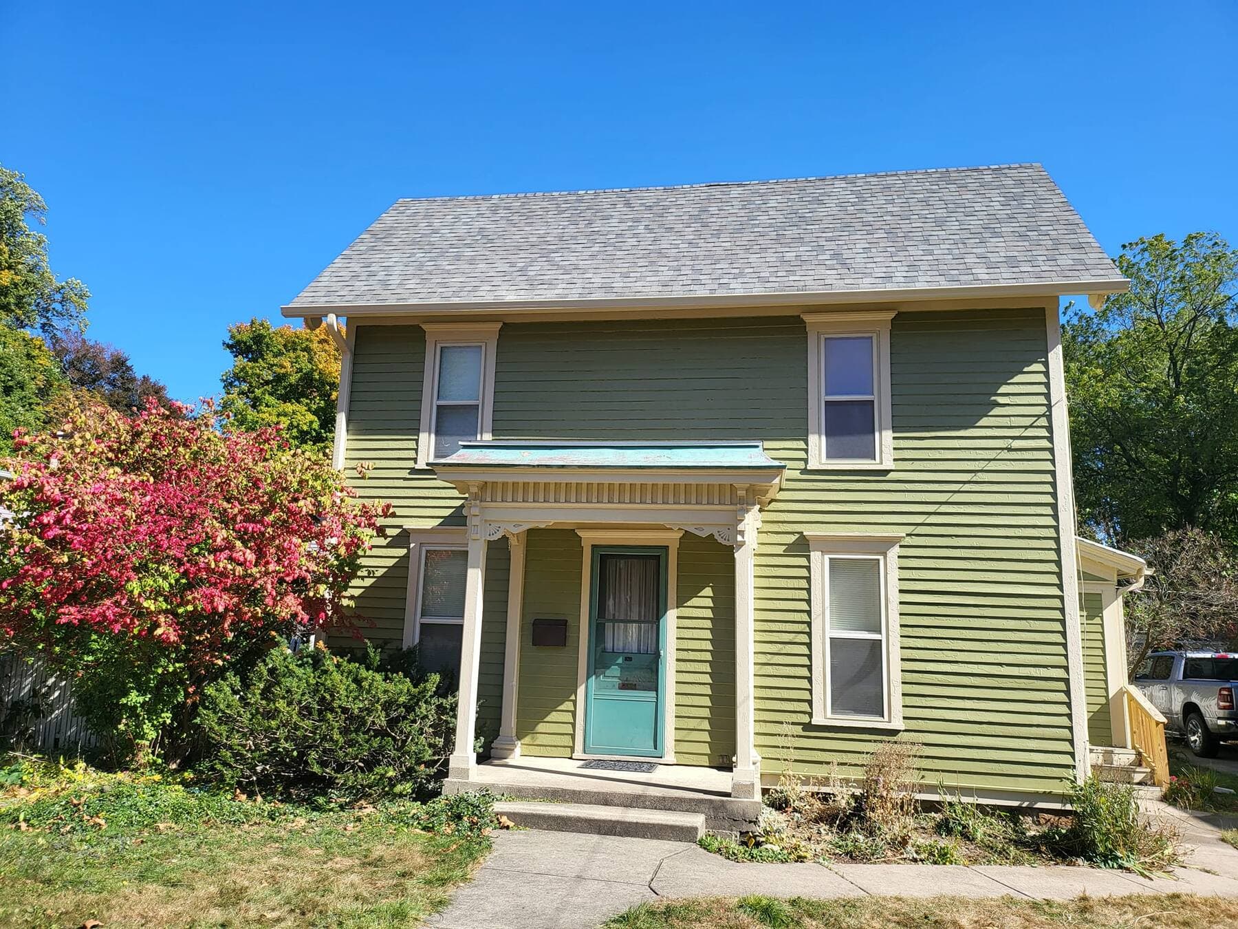 Same Victorian home painted olive green photographed straight on from the front showing the centered porch and teal door, exterior painting by Fortoso Painting in Southwest Michigan